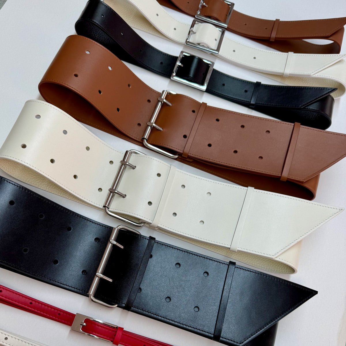 Aria Margo collection of wide Italian leather military coat belts in black, white, and brown with silver buckles.