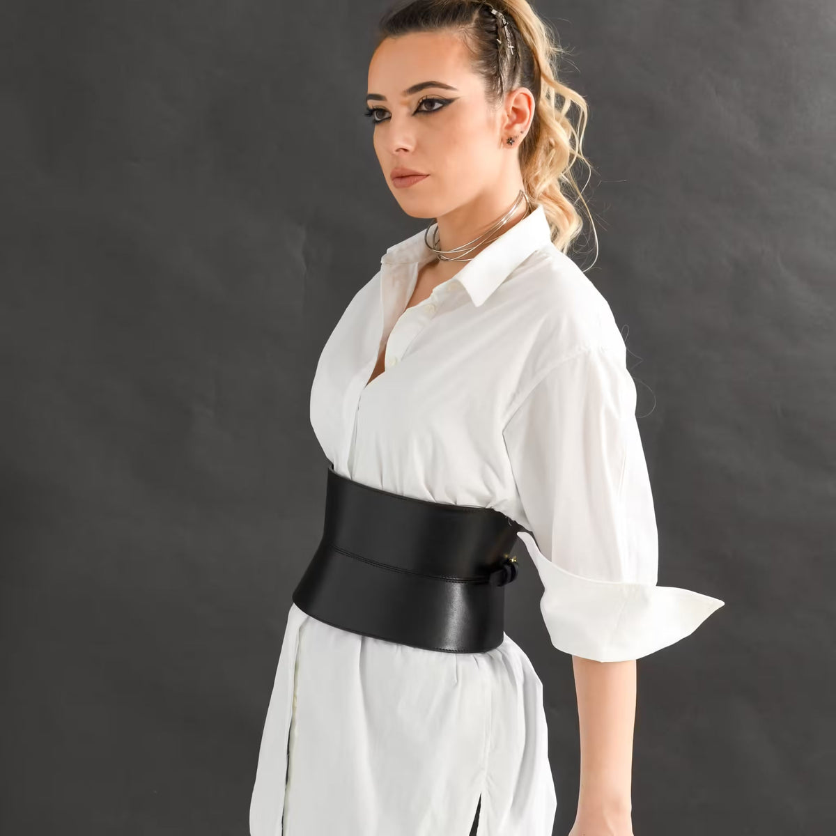 Aria Margo wide black leather corset belt worn over a crisp white shirt, creating an hourglass silhouette.