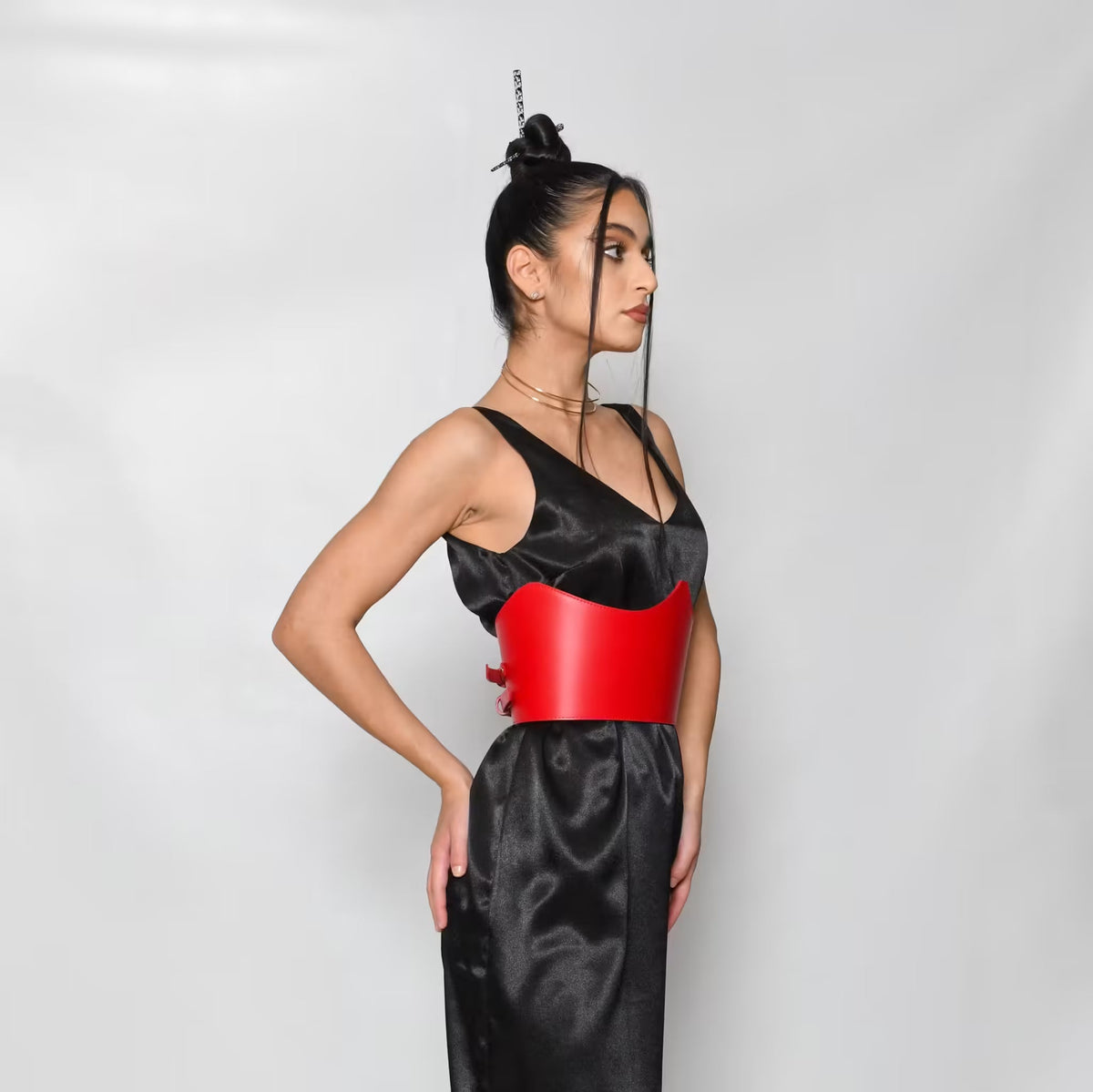 Aria Margo red Italian leather under-bust belt worn over a black satin dress by a model in profile view.