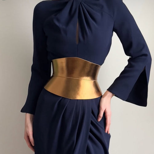 Aria Margo gold metallic Italian leather corset belt with an hourglass silhouette worn over a navy blue dress.