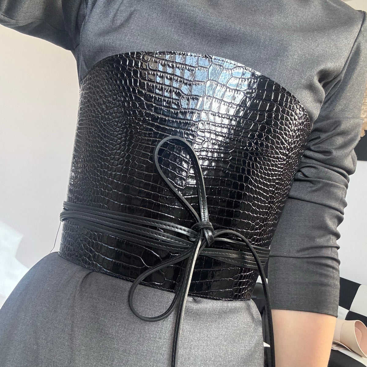 Aria Margo black croc-embossed leather corset belt with wrap-around cord lacing worn over a grey dress