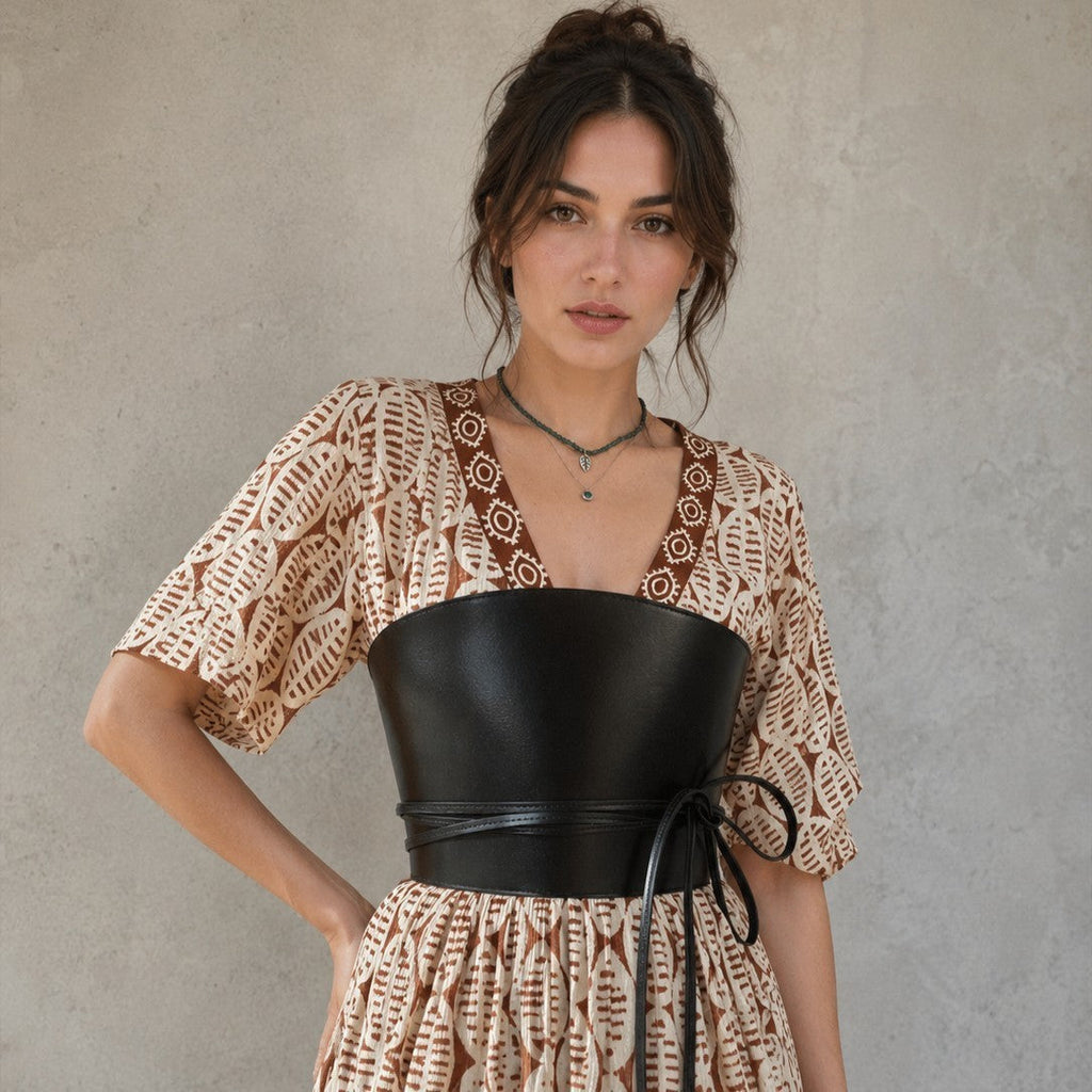 Aria Margo black leather corset belt with wrap-around cord detail worn over a patterned beige dress.