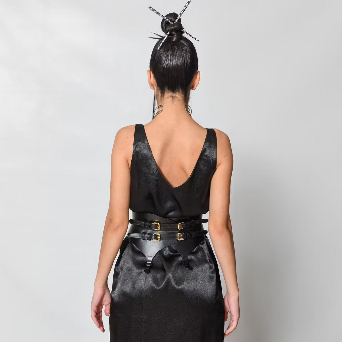 Aria Margo black leather corset belt with gold buckles and garter tabs worn over a black satin dress, back view
