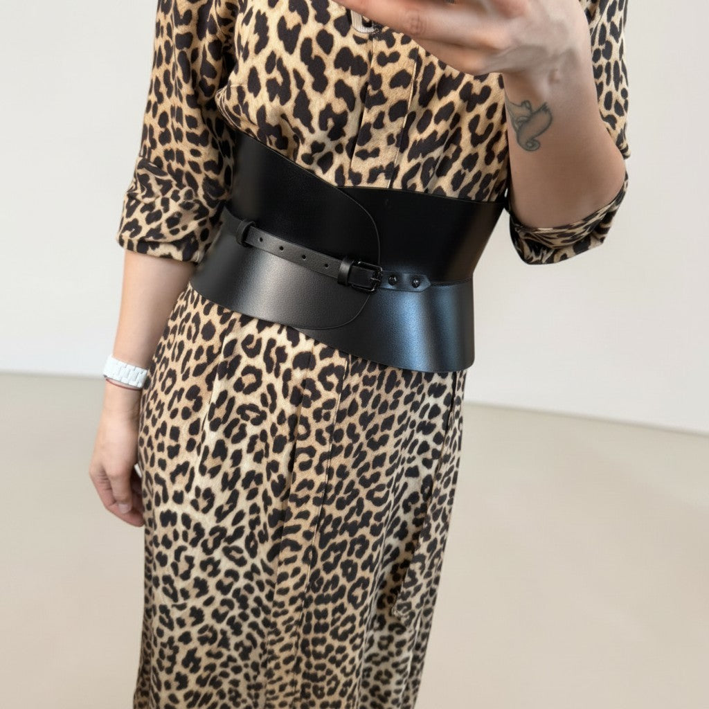Aria Margo black leather hourglass corset belt worn over a leopard print dress to define the waist.