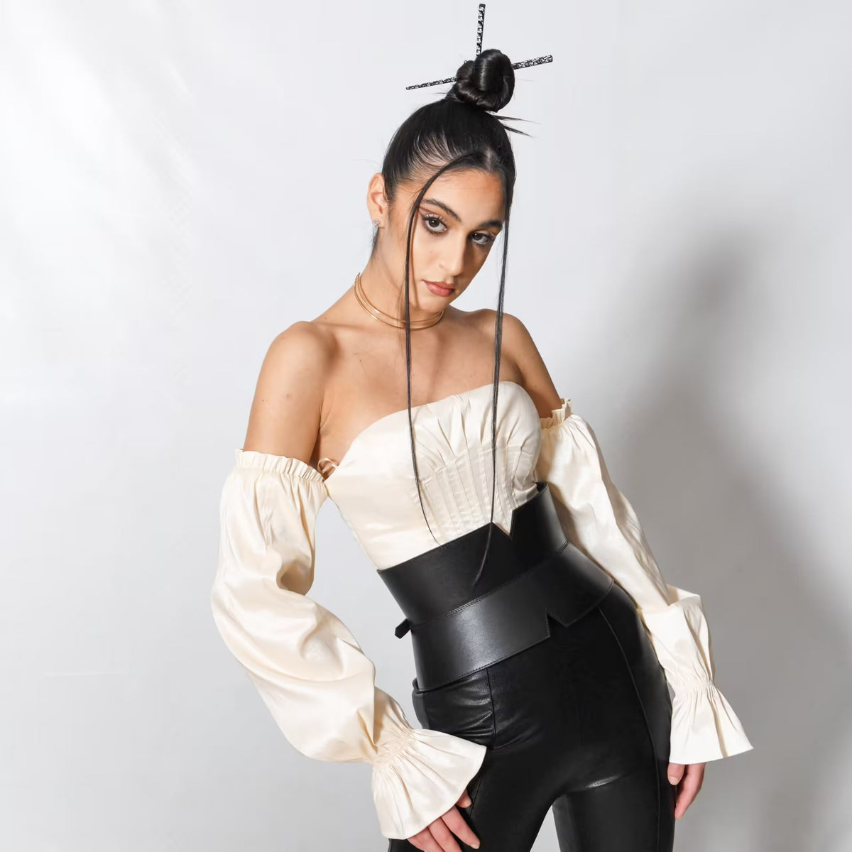 Aria Margo black leather V-cut corset belt worn over a cream off-shoulder top and black leather trousers