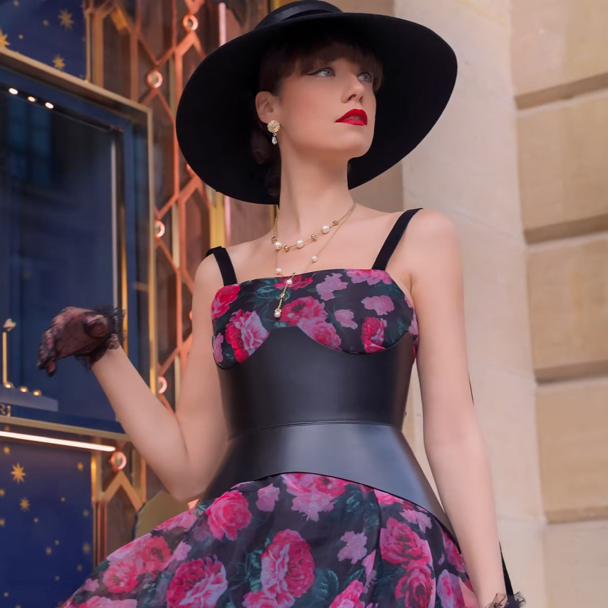 Aria Margo black leather XO corset belt worn over a floral dress by a model in a wide-brimmed hat