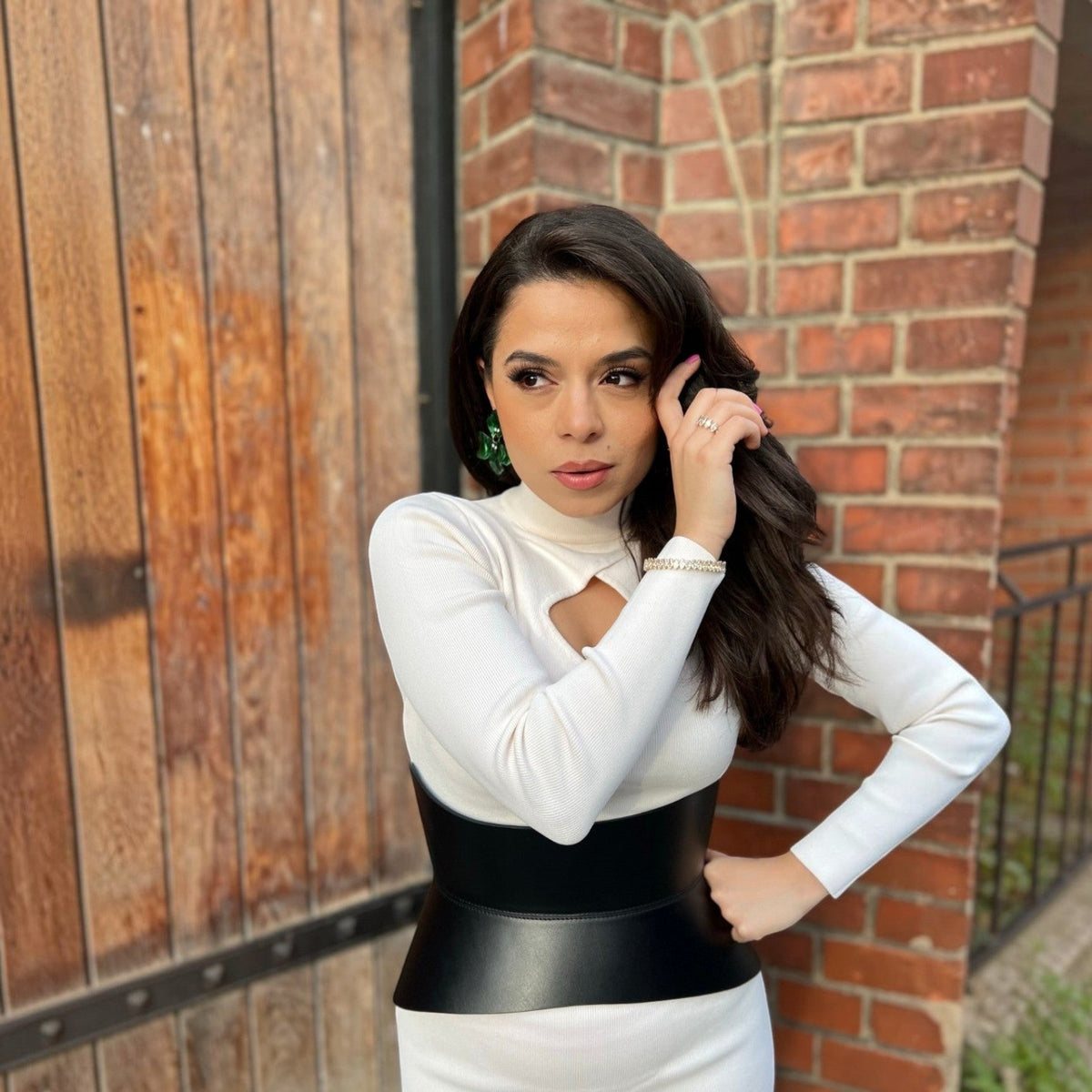 Aria Margo black Italian leather corset belt worn over a white long-sleeve top against a brick wall background.