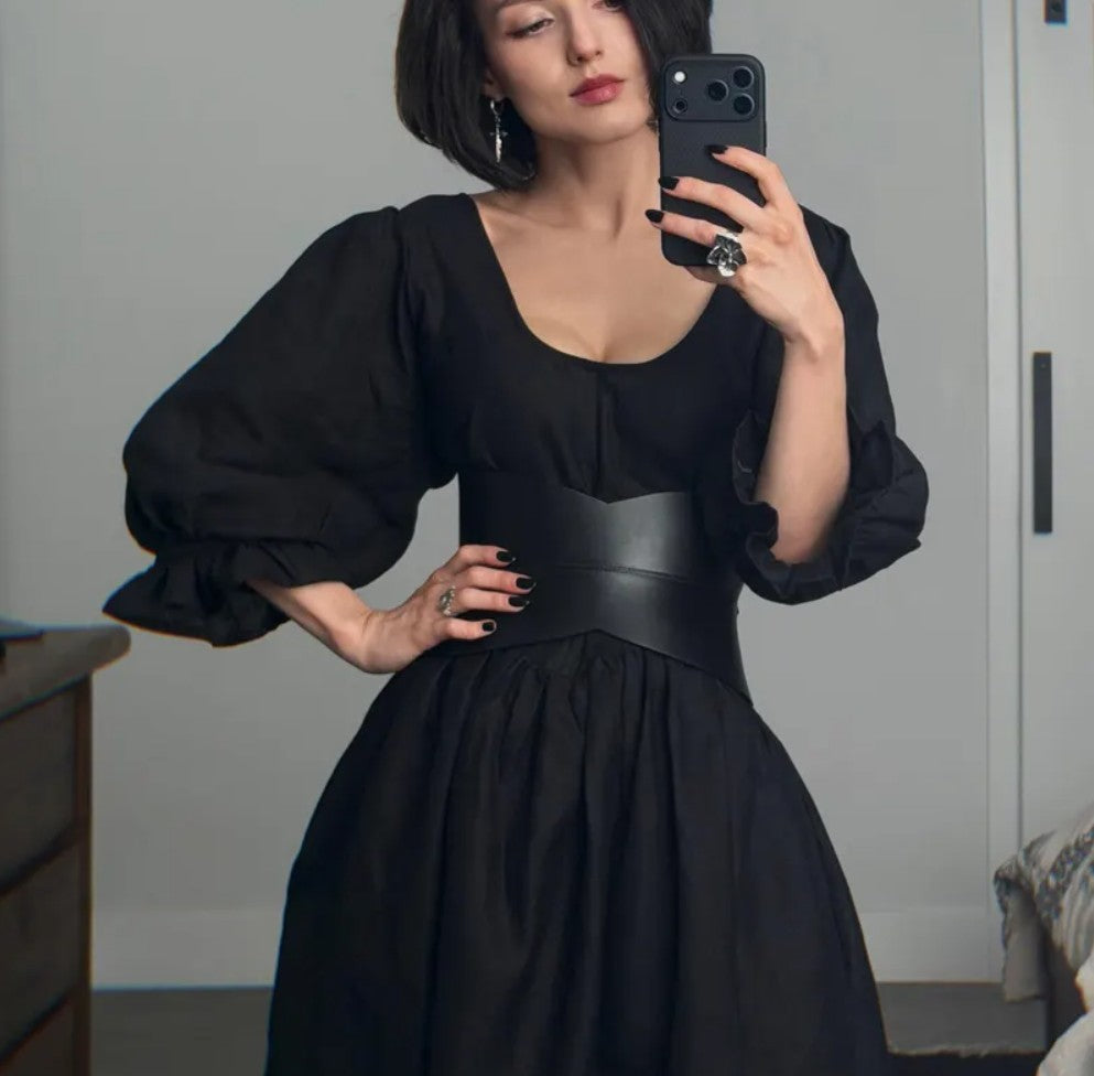 Aria Margo black leather hourglass corset belt worn over a black puff-sleeve dress for a defined waist silhouette.