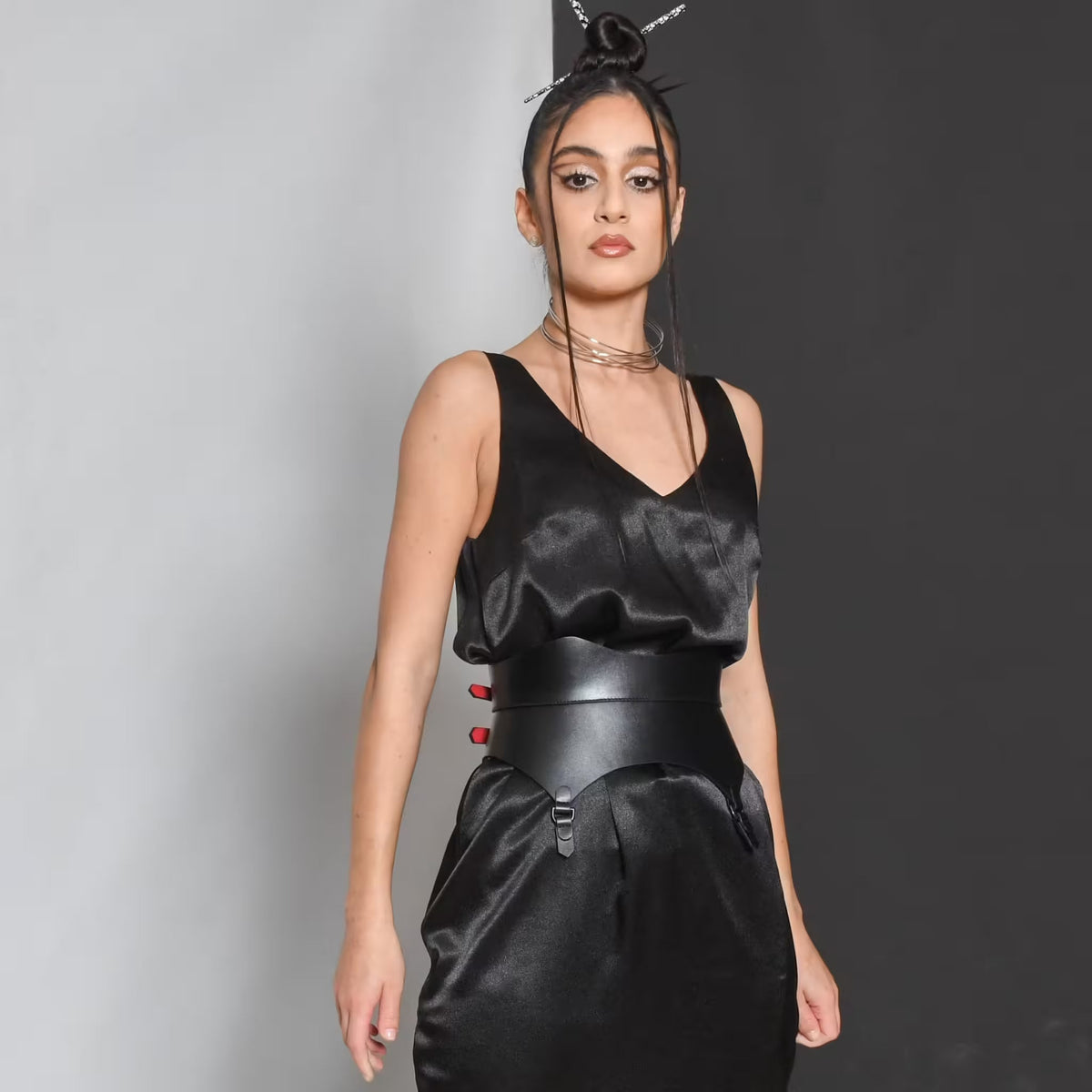 Aria Margo black leather corset belt with gold buckles and red accents worn over a black satin dress