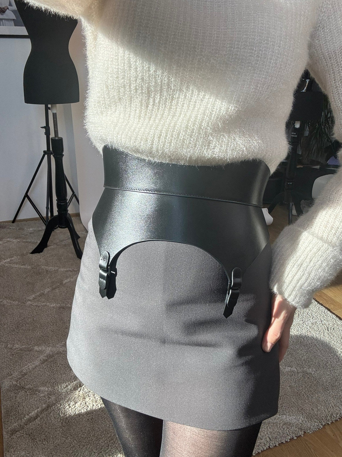 Aria Margo black leather corset belt with garter-style tabs worn over a white sweater and grey skirt