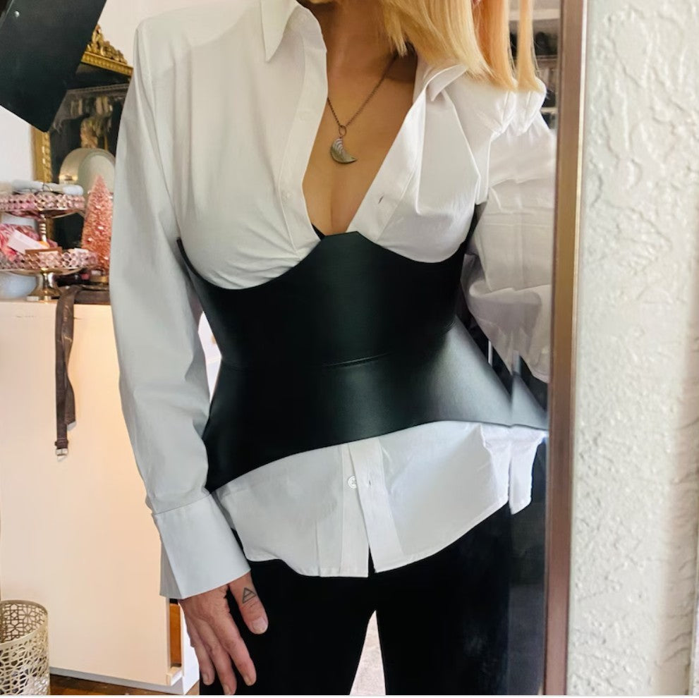Aria Margo black leather corset belt worn over a white button-down shirt to create an hourglass silhouette.