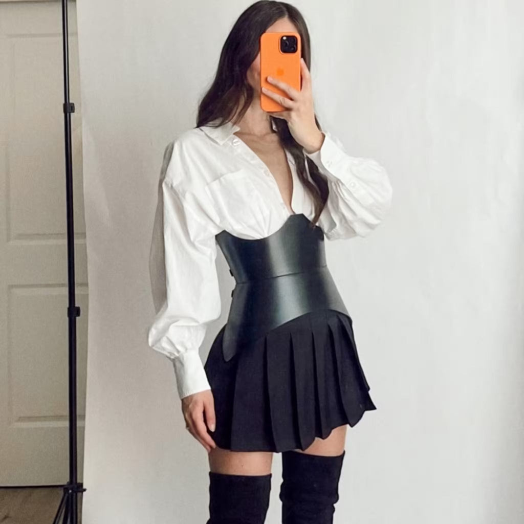 Aria Margo black leather XO corset belt worn over a white oversized shirt and black pleated skirt