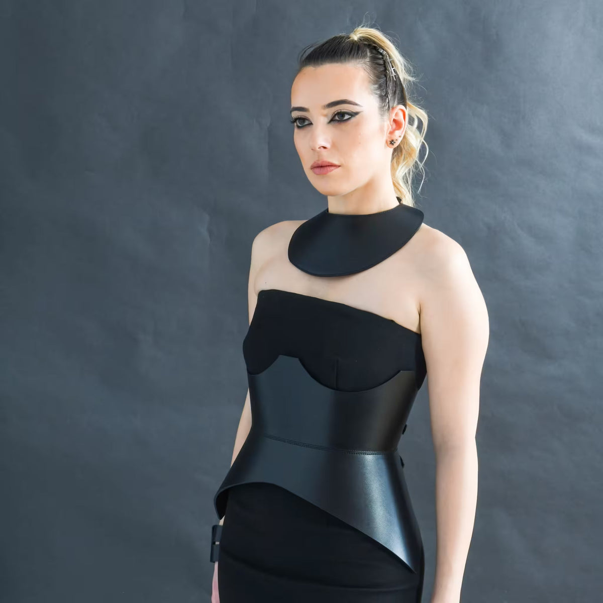 Aria Margo black leather corset belt worn over a matching dress, highlighting a sculpted hourglass silhouette.