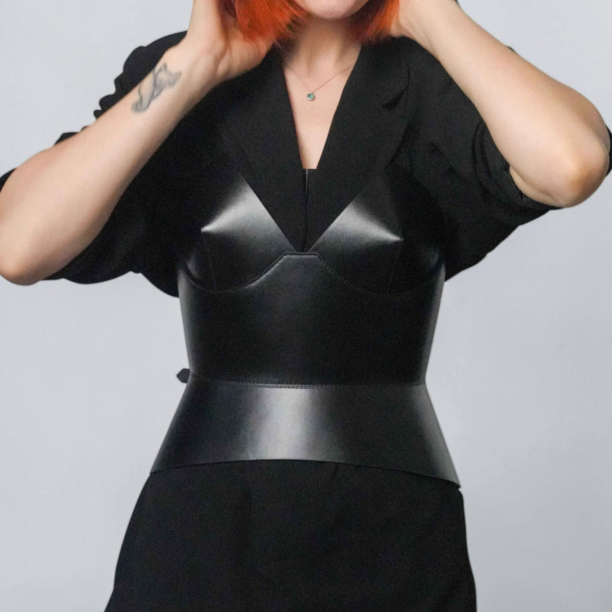 Aria Margo black leather round body corset worn over a black blazer by a woman with short red hair