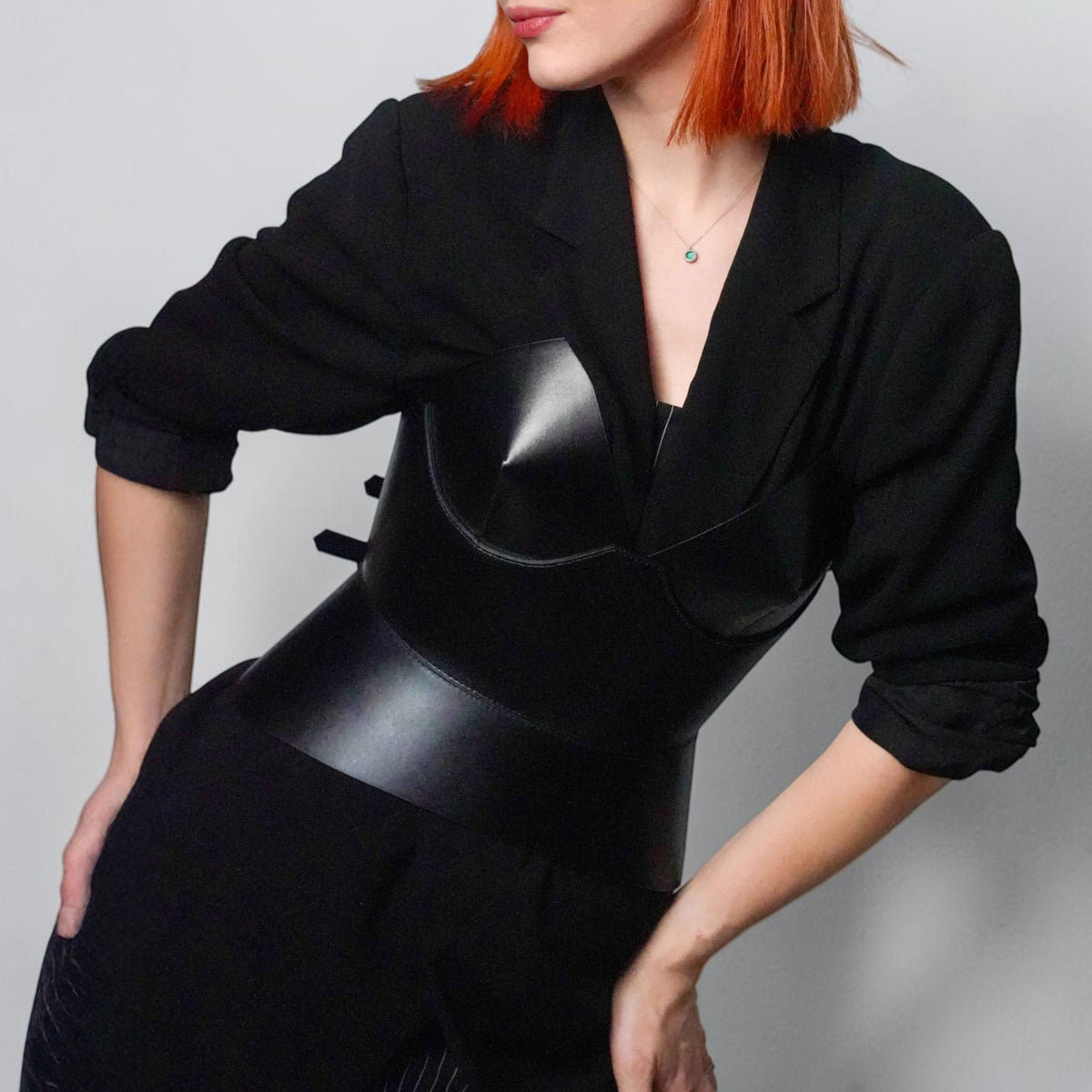Aria Margo black leather round body corset worn over a black blazer by a woman with short red hair