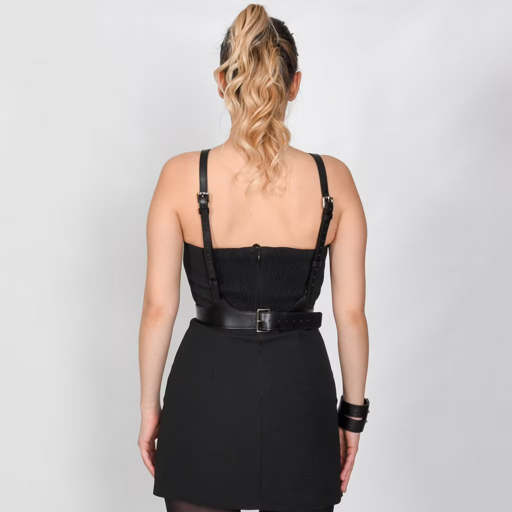 Aria Margo black leather V-neck harness belt worn over a black dress, showing the suspender effect on the back.