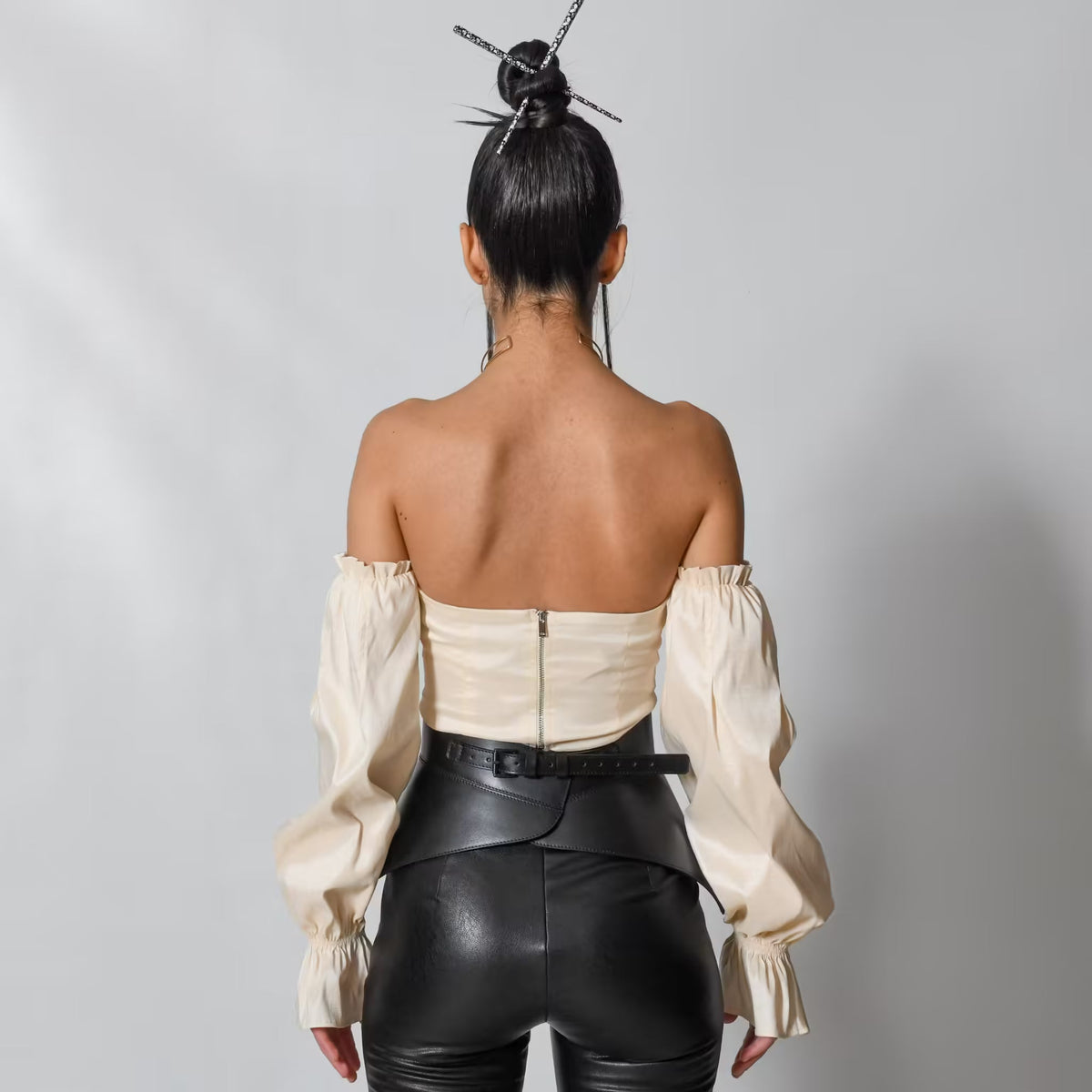 Aria Margo black leather peplum corset belt worn over a cream off-shoulder top, back view.