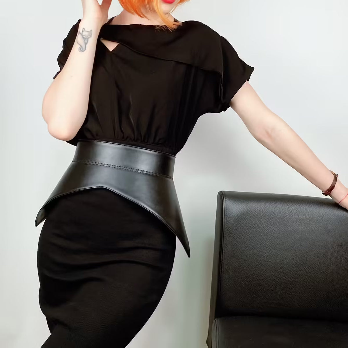 Aria Margo black leather peplum corset belt worn over a black dress to accentuate the waist and hips.