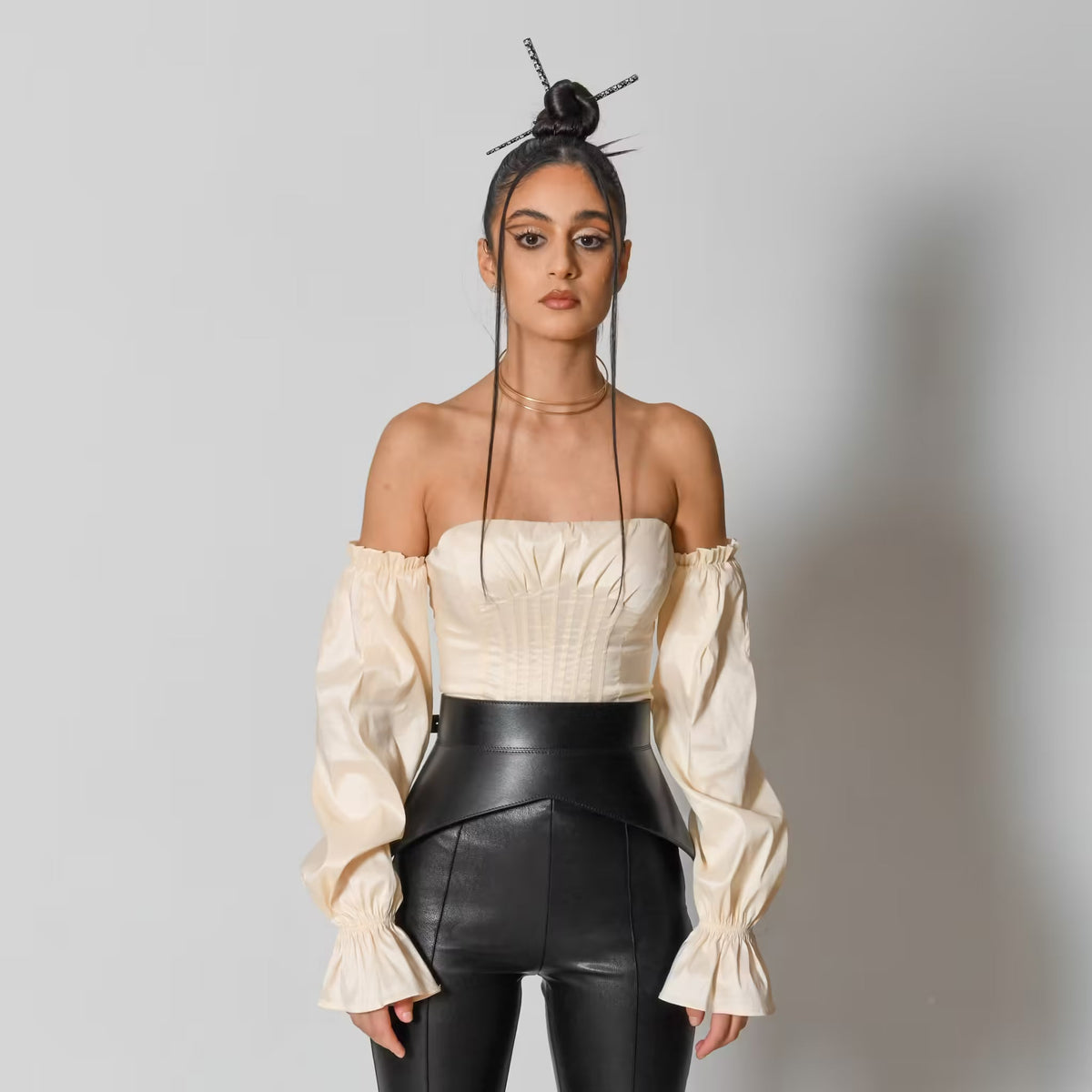 Aria Margo black leather peplum corset belt worn over a cream off-shoulder top and black trousers