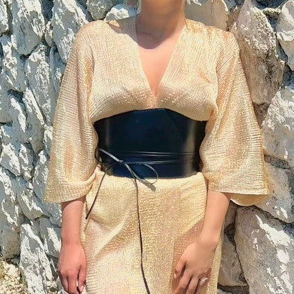 Aria Margo black leather under-bust belt worn over a gold textured dress, featuring a wrap-around cord design.