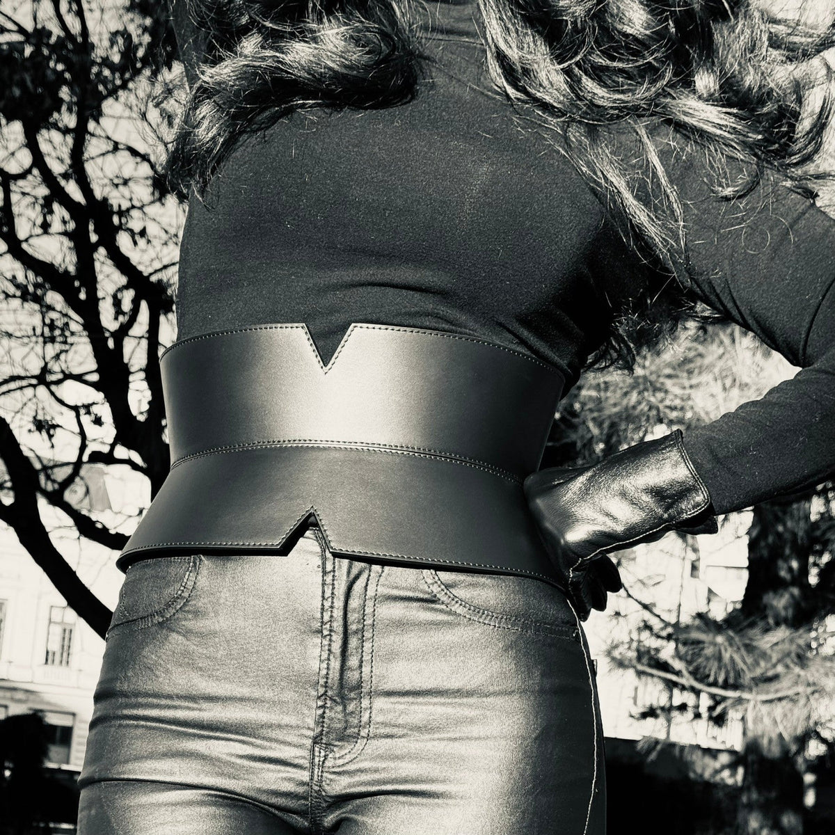 Aria Margo black leather V-cut corset belt worn over a black top and trousers to define the waistline