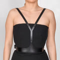 Aria Margo black leather V-neck harness belt worn over a black strapless dress to frame the upper body.