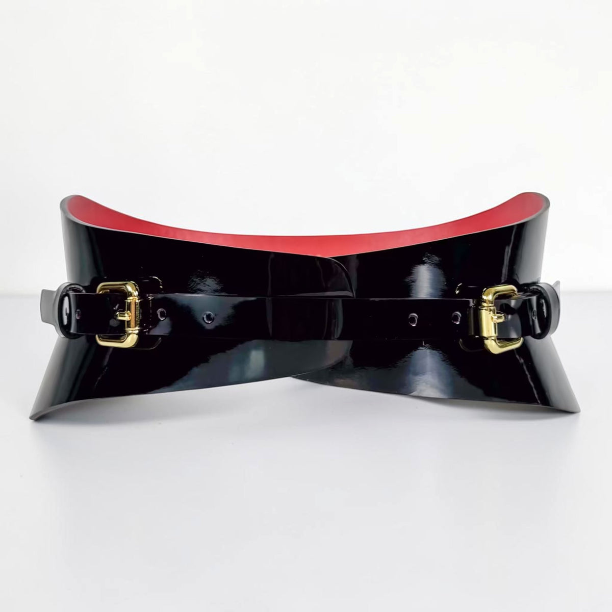 Aria Margo black patent leather slim corset belt with gold buckles and a contrasting red interior lining.