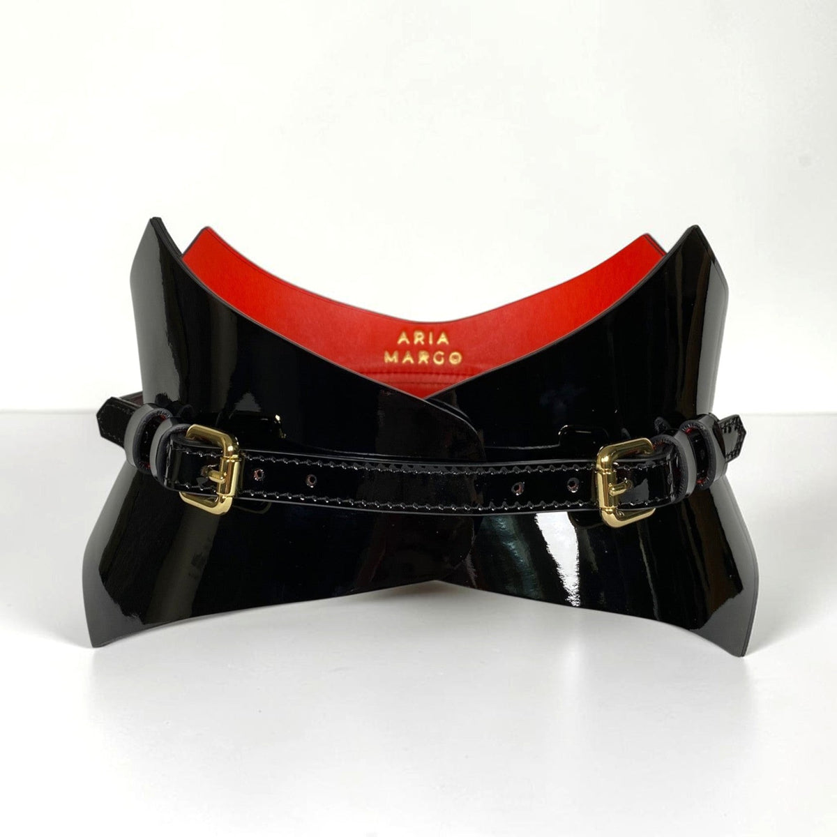 Aria Margo black patent leather corset belt with gold buckles and a vibrant red interior lining.