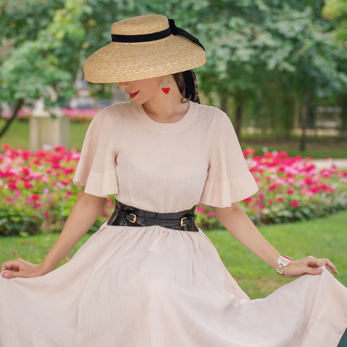 Aria Margo slim black patent leather corset belt worn over a light beige dress in a garden setting