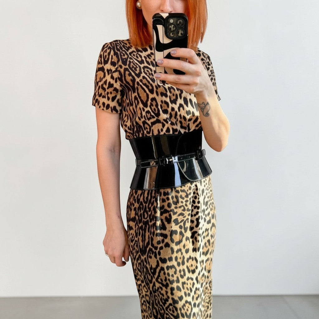 Aria Margo wide black patent leather corset belt worn over a leopard print dress for a defined hourglass shape.