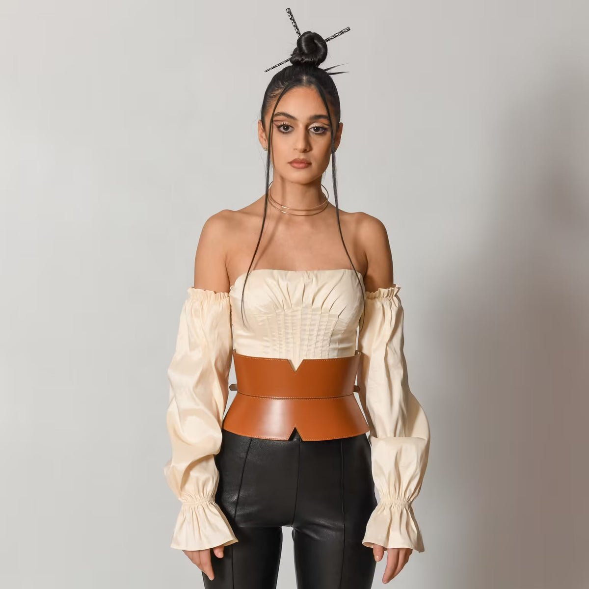 Aria Margo brown leather V-cut corset belt worn over a cream off-shoulder top and black trousers