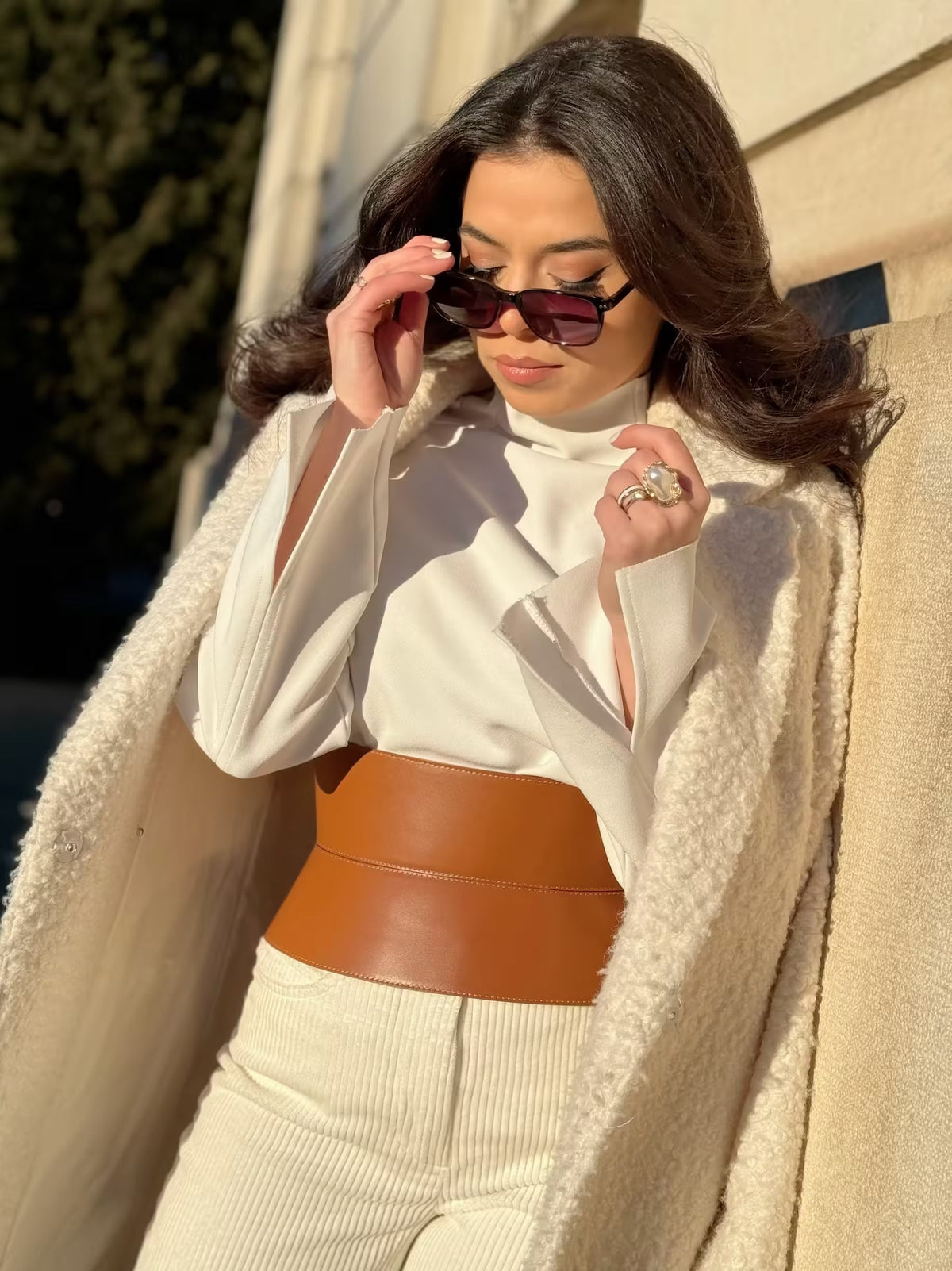 Aria Margo wide brown Italian leather corset belt worn over a white turtleneck and cream coat for waist shaping.