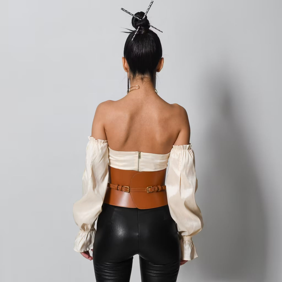 Aria Margo brown leather V-cut corset belt worn over a cream off-shoulder top and black trousers, back view.