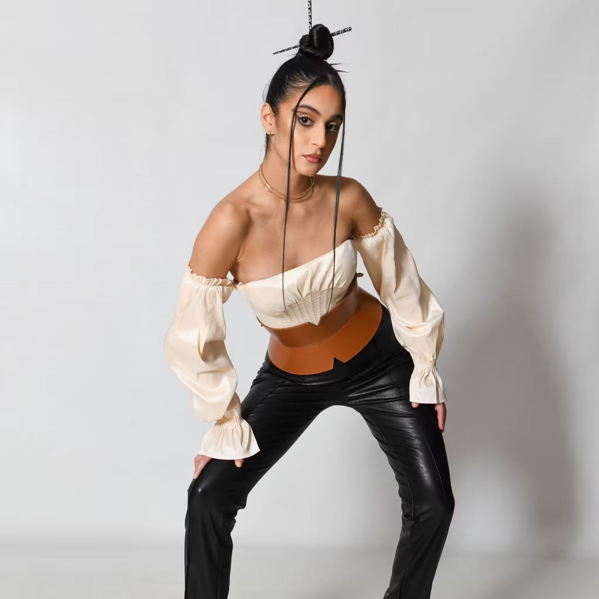 Aria Margo brown leather V-cut corset belt worn by a model in a cream off-shoulder top and black trousers