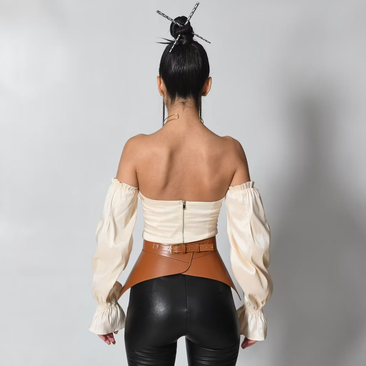 Aria Margo brown leather peplum corset belt worn over a cream off-shoulder top and black trousers, back view.