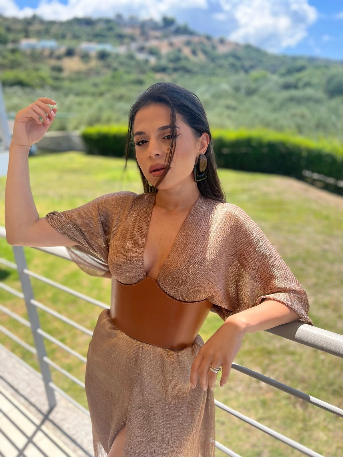 Aria Margo brown leather under-bust belt worn over a shimmering gold dress by a woman outdoors.