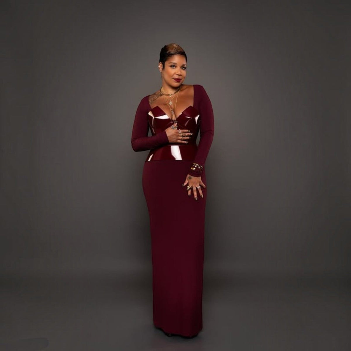 Aria Margo burgundy patent leather corset worn over a long-sleeved dress, highlighting a feminine silhouette.