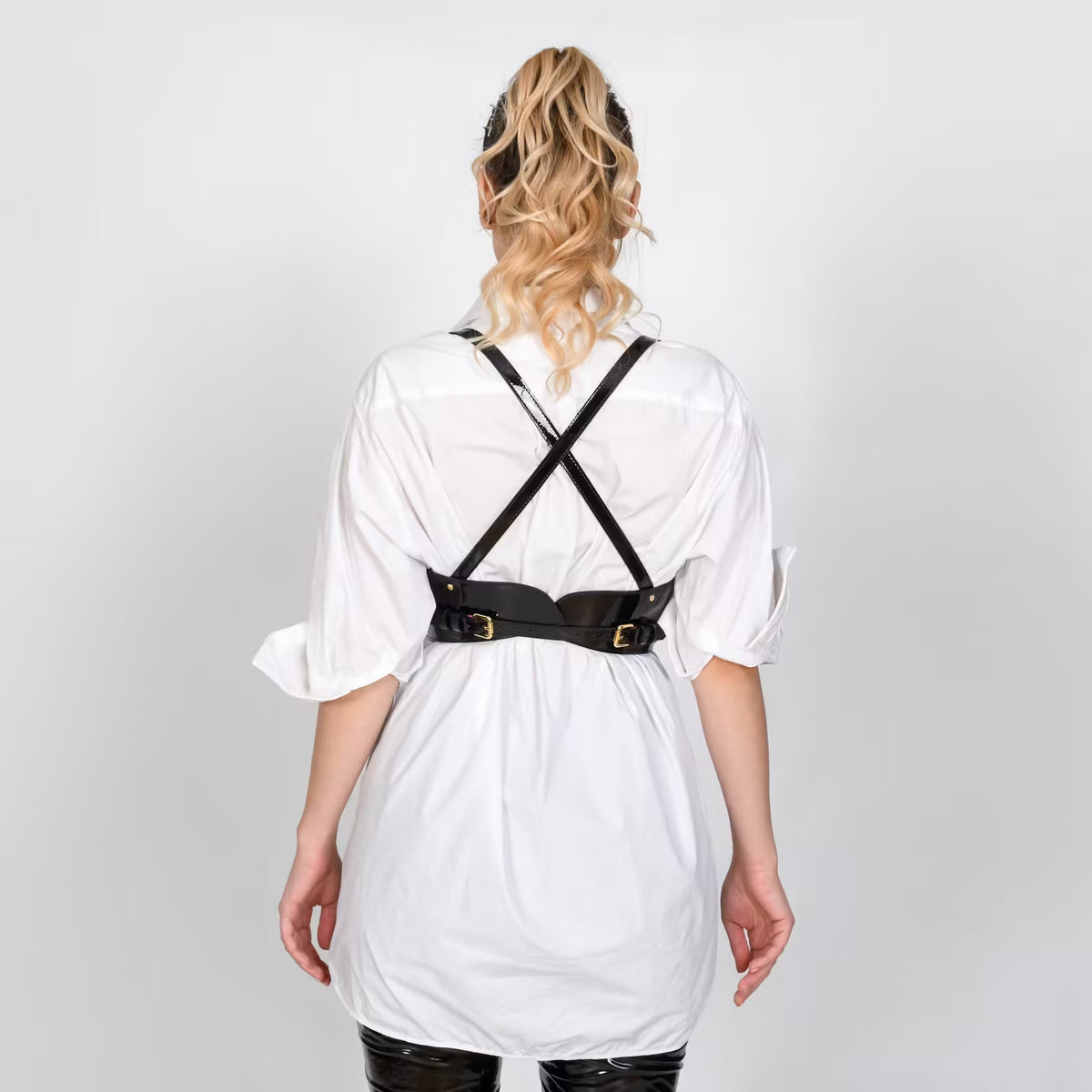Back view of Aria Margo black patent leather under-bust belt with adjustable straps over a white shirt.