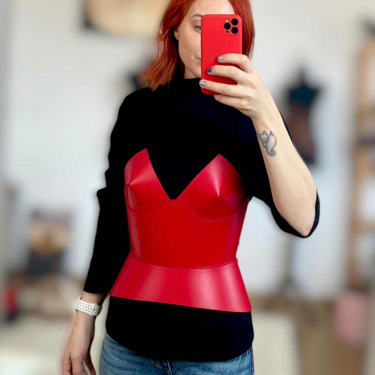 Aria Margo red leather corset belt worn over a black long-sleeve top to create a structured feminine silhouette.