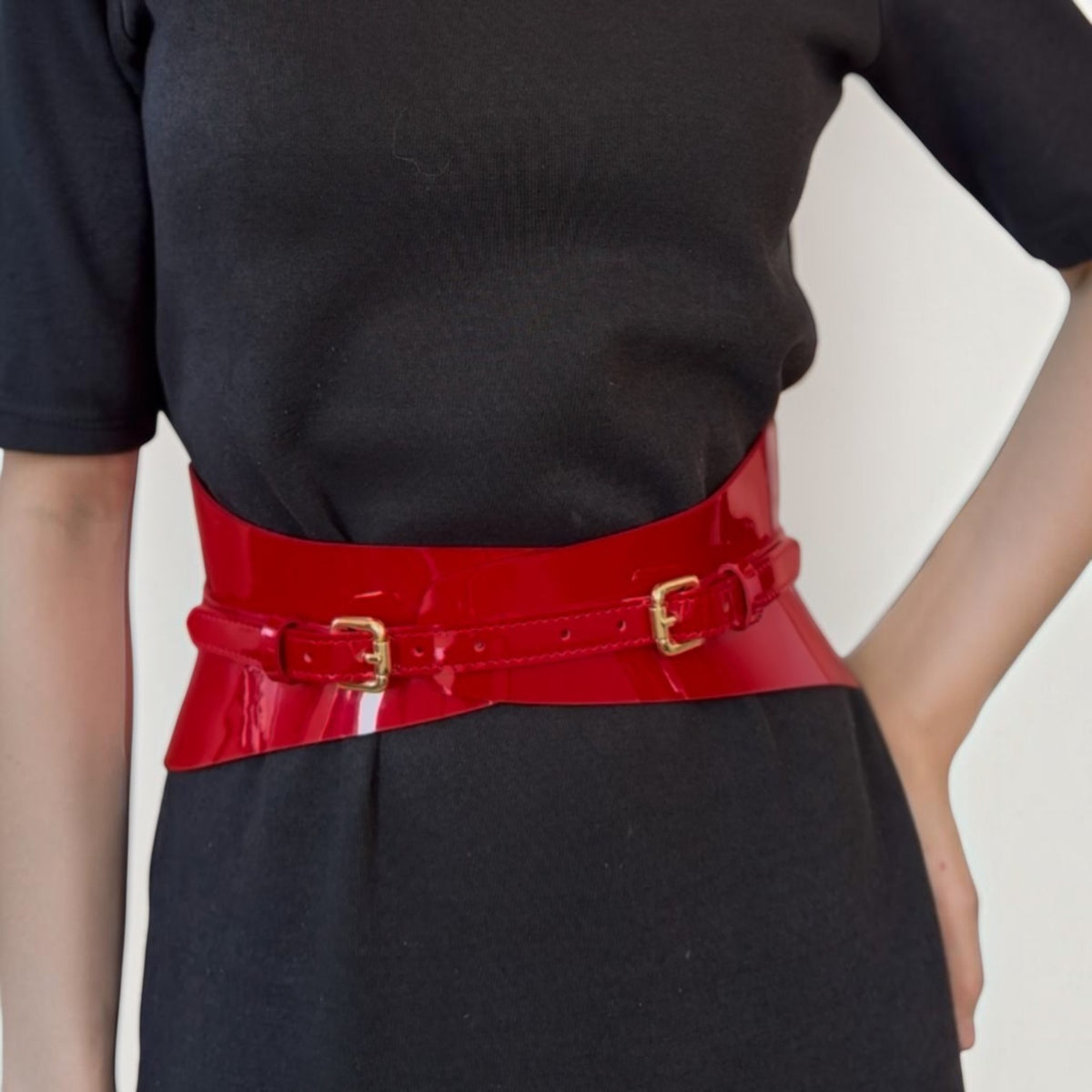Aria Margo slim red patent leather corset belt with gold buckles worn over a black dress