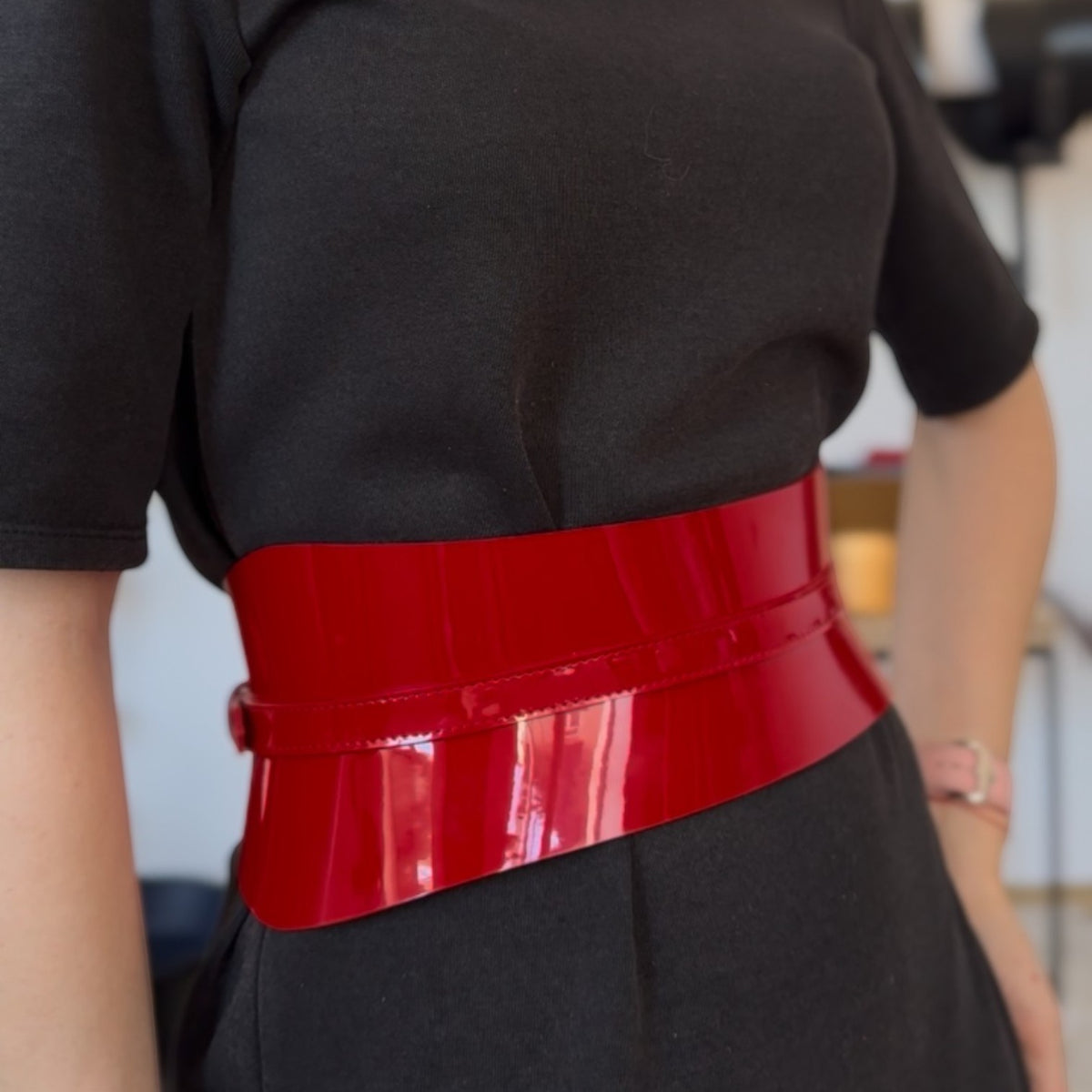 Aria Margo slim red patent leather corset belt worn over a black dress for a structured waistline