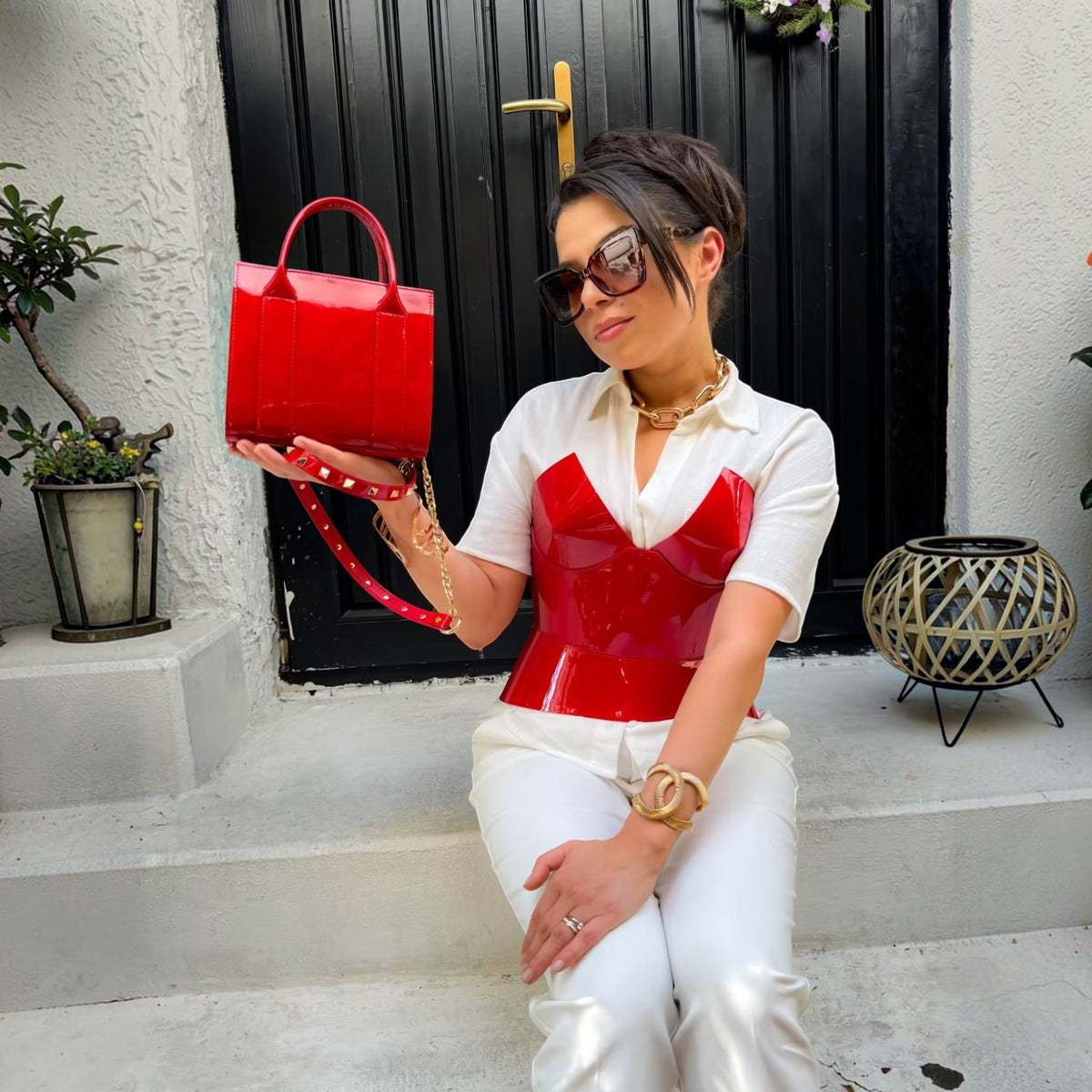 Aria Margo red patent leather corset worn over a white shirt with a matching red patent handbag