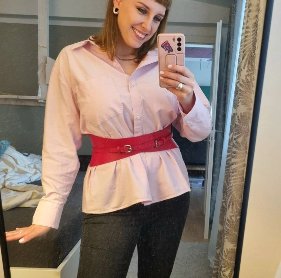 Aria Margo slim red Italian leather corset belt worn over a light pink button-down shirt and dark trousers