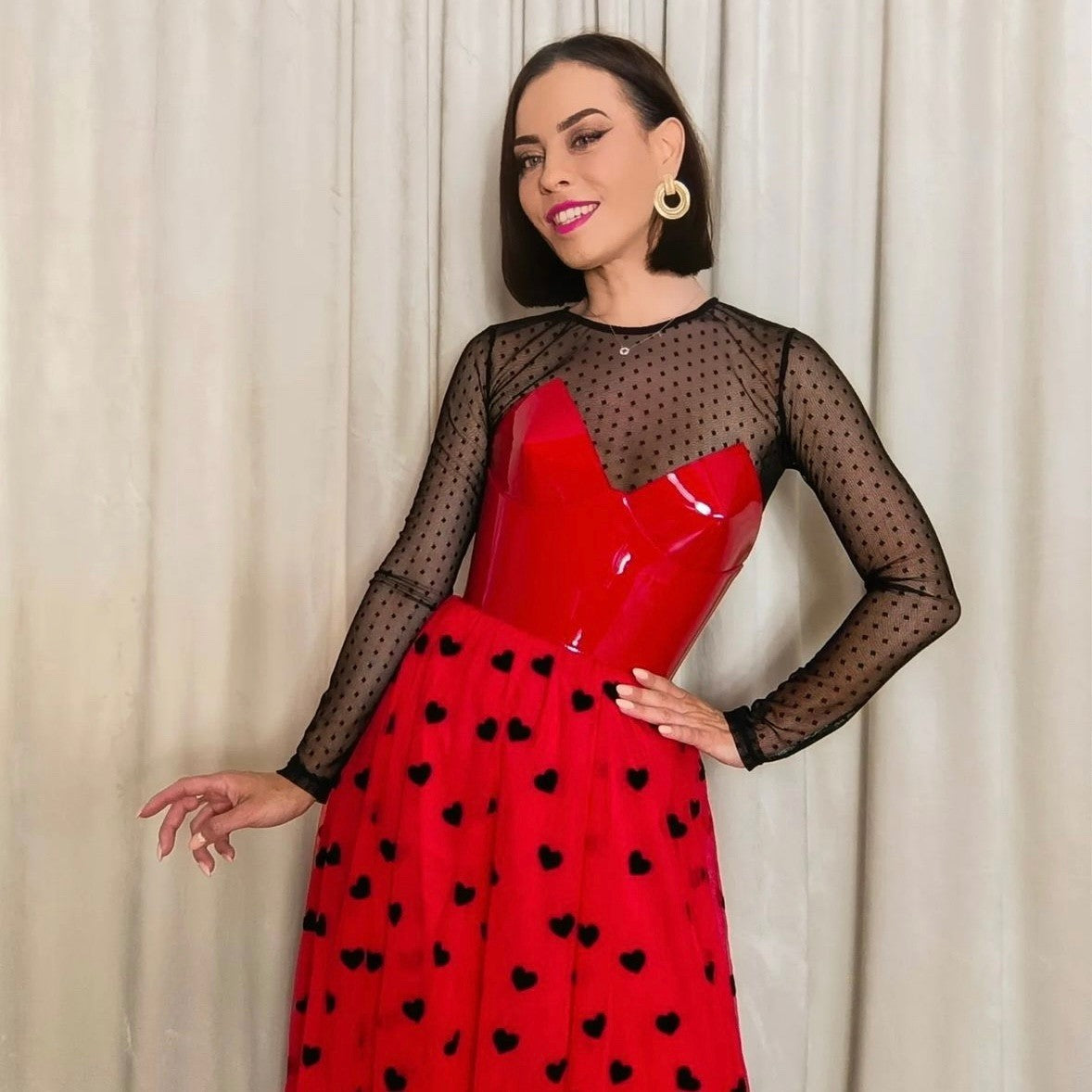 Aria Margo red patent leather over-bust corset worn over a black sheer polka dot top and red heart-print skirt.