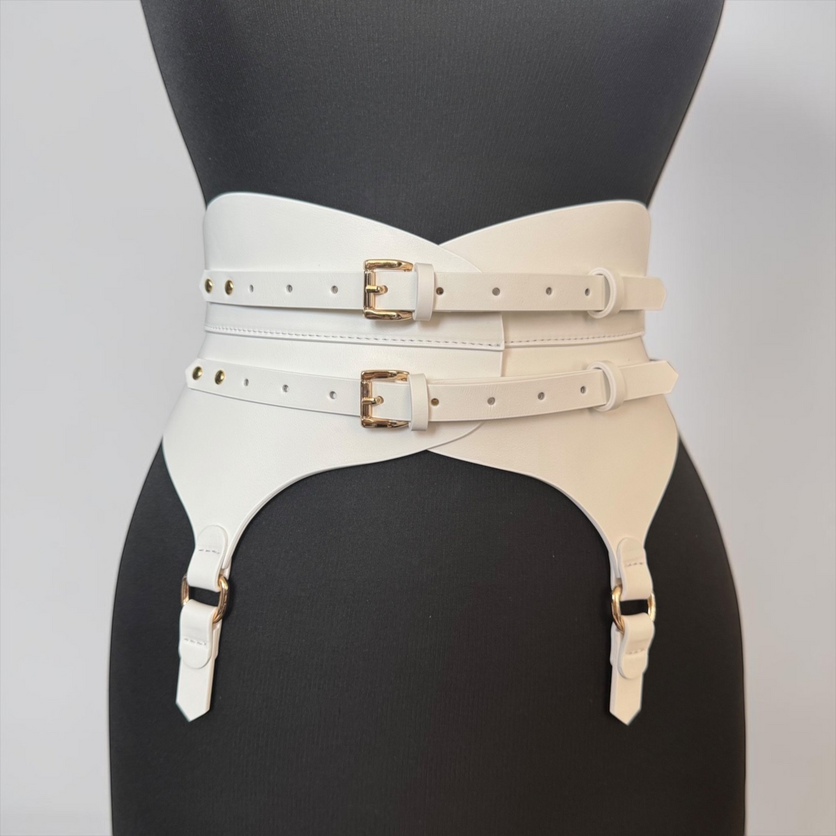 Aria Margo white Italian leather corset belt with gold buckles and garter straps on a black mannequin torso.